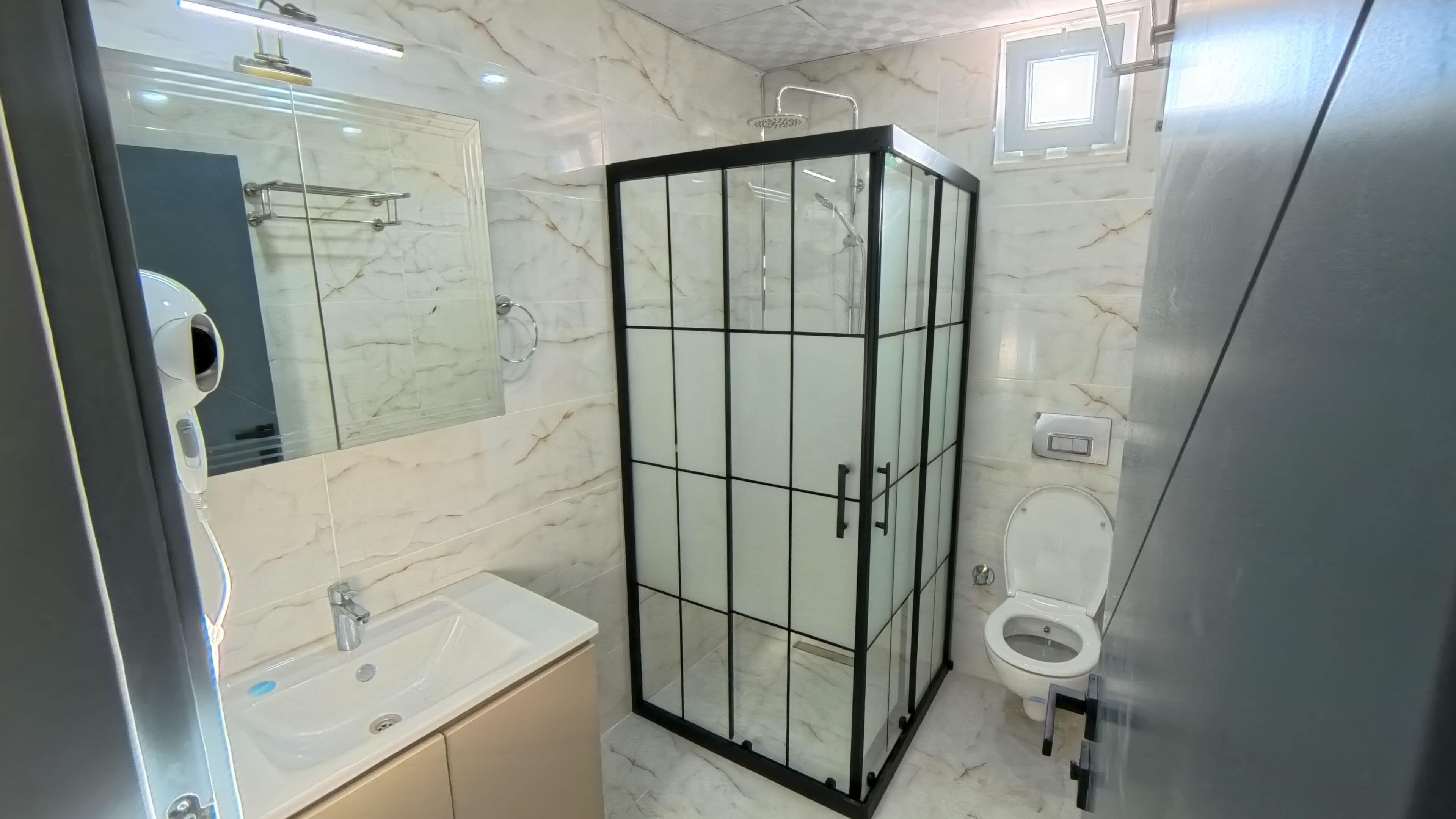 Un bany amb plat de dutxa tancat amb vidre, un lavabo i un vàter.
