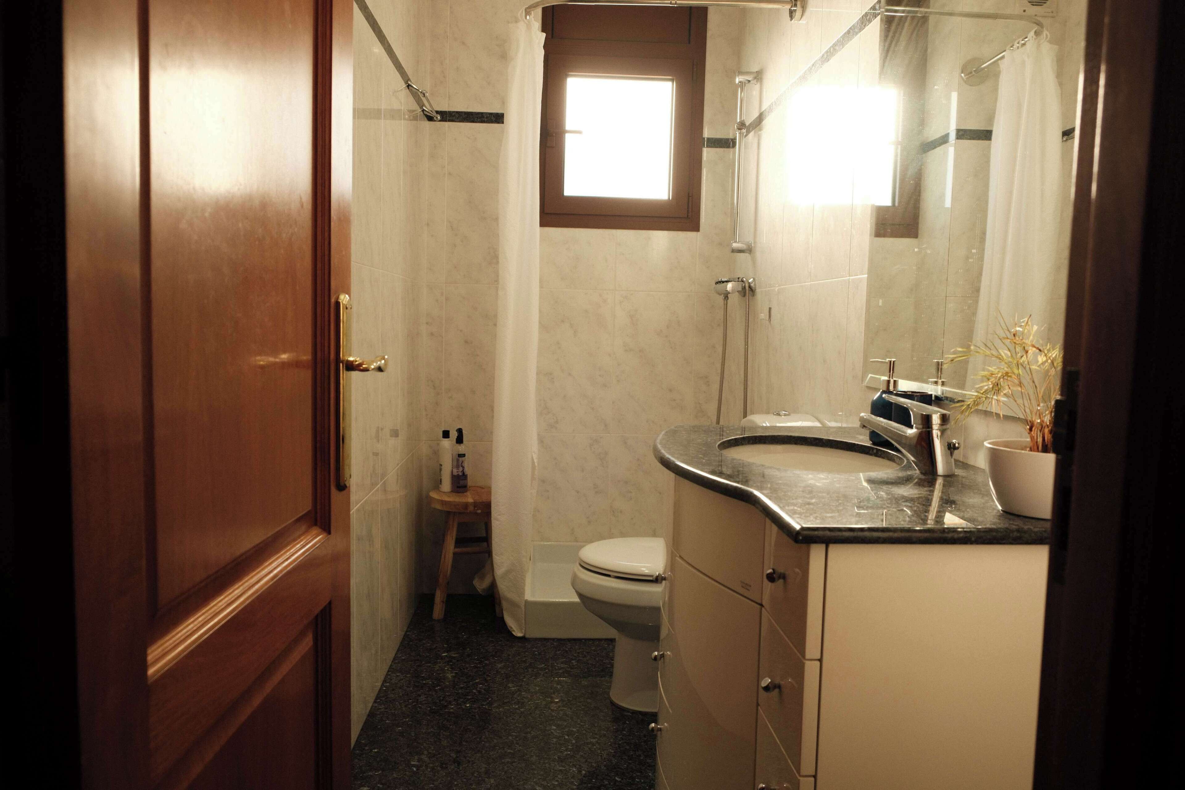 A bathroom with a wooden door, a toilet, a sink, and a shower.