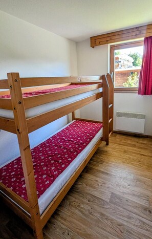 A bunk bed with a red patterned mattress in a room with wooden flooring and a window with a red curtain.