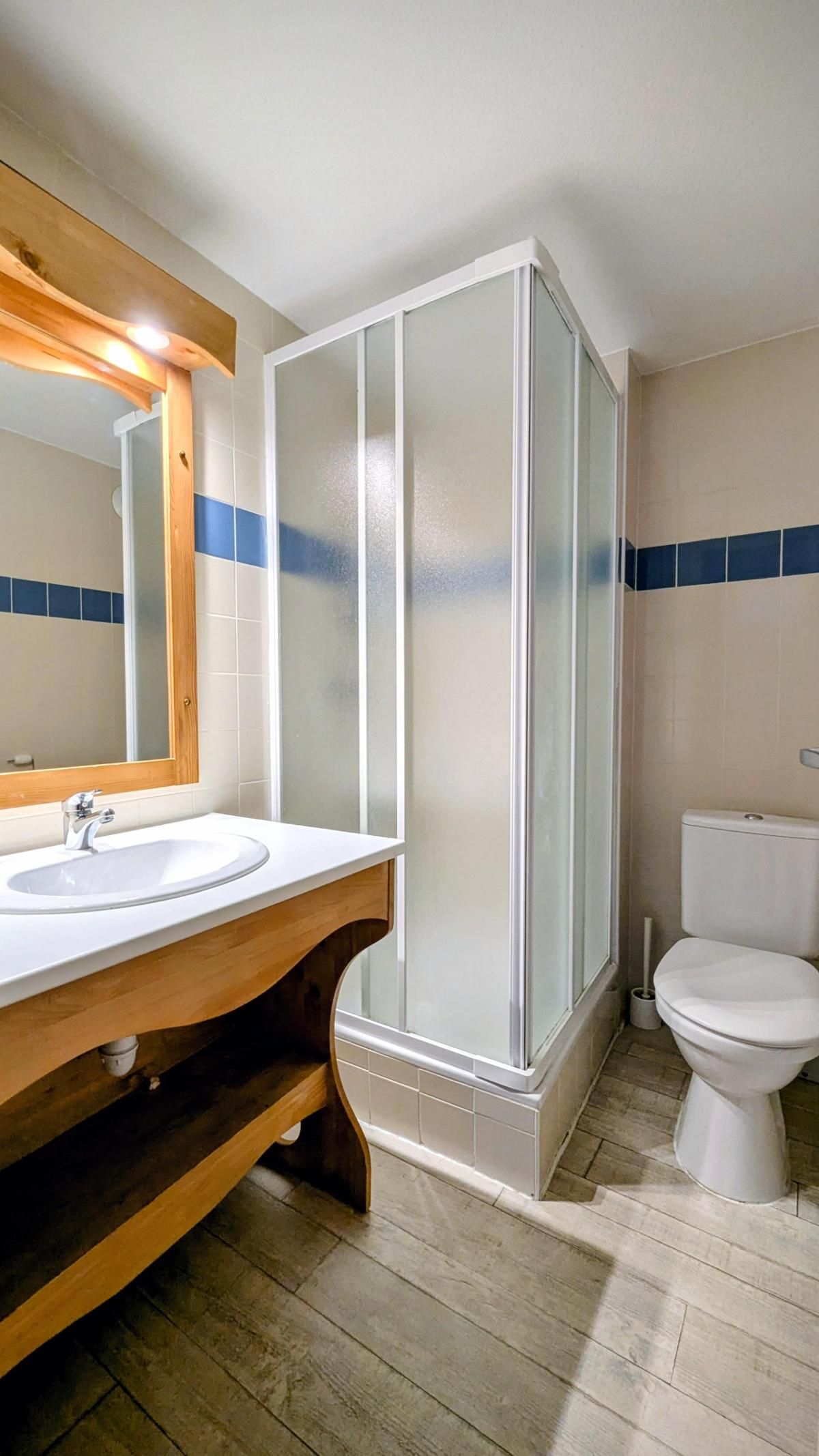 Une salle de bain avec un meuble-lavabo en bois, un lavabo blanc, un miroir, une cabine de douche en verre et des toilettes.