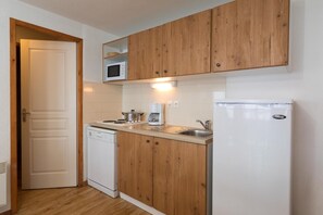 A compact kitchen with wooden cabinets, a microwave, a coffee maker, a dishwasher, and a refrigerator.