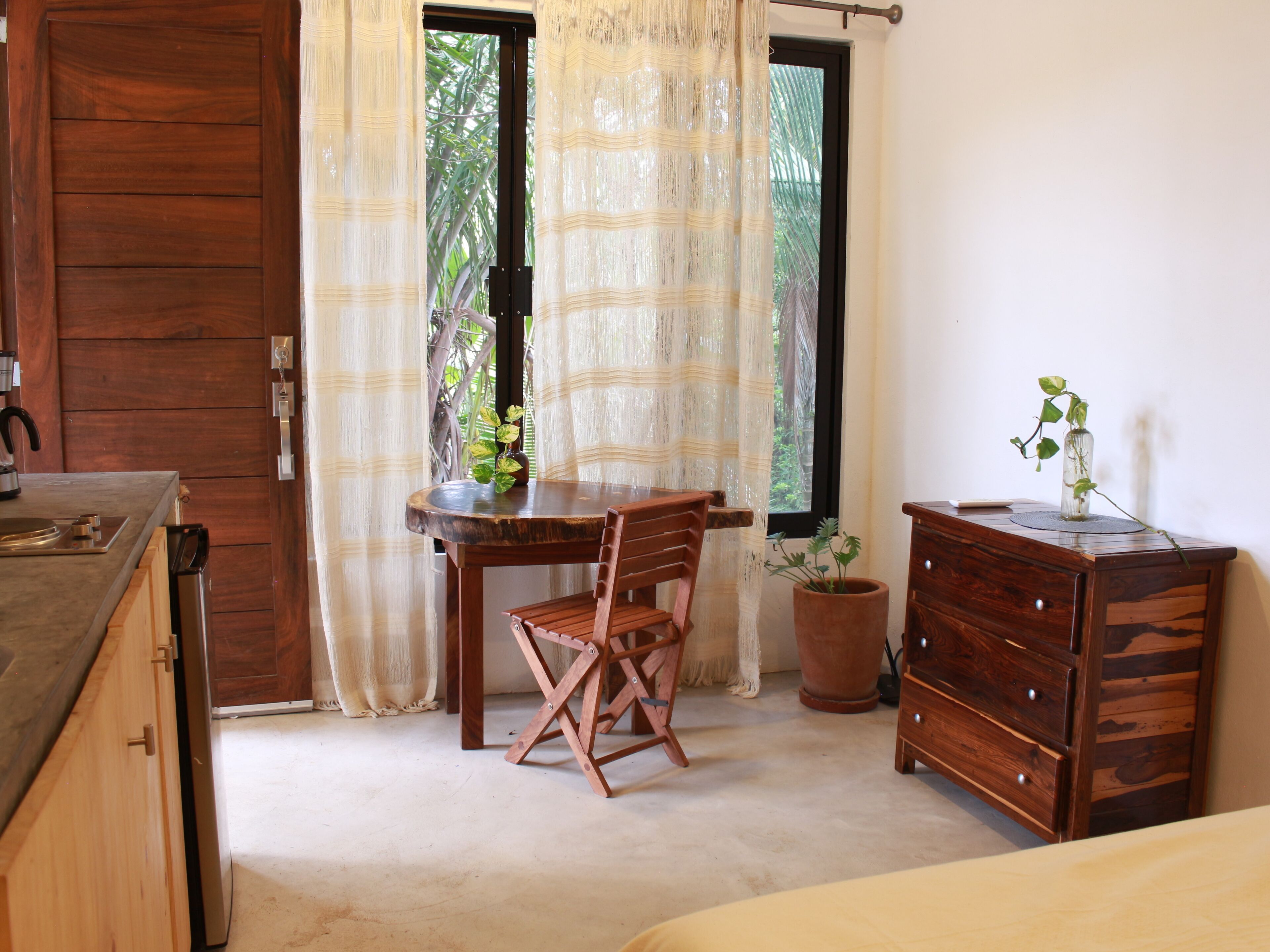 A room with a wooden door, a table with a chair, a potted plant, and a wooden dresser.