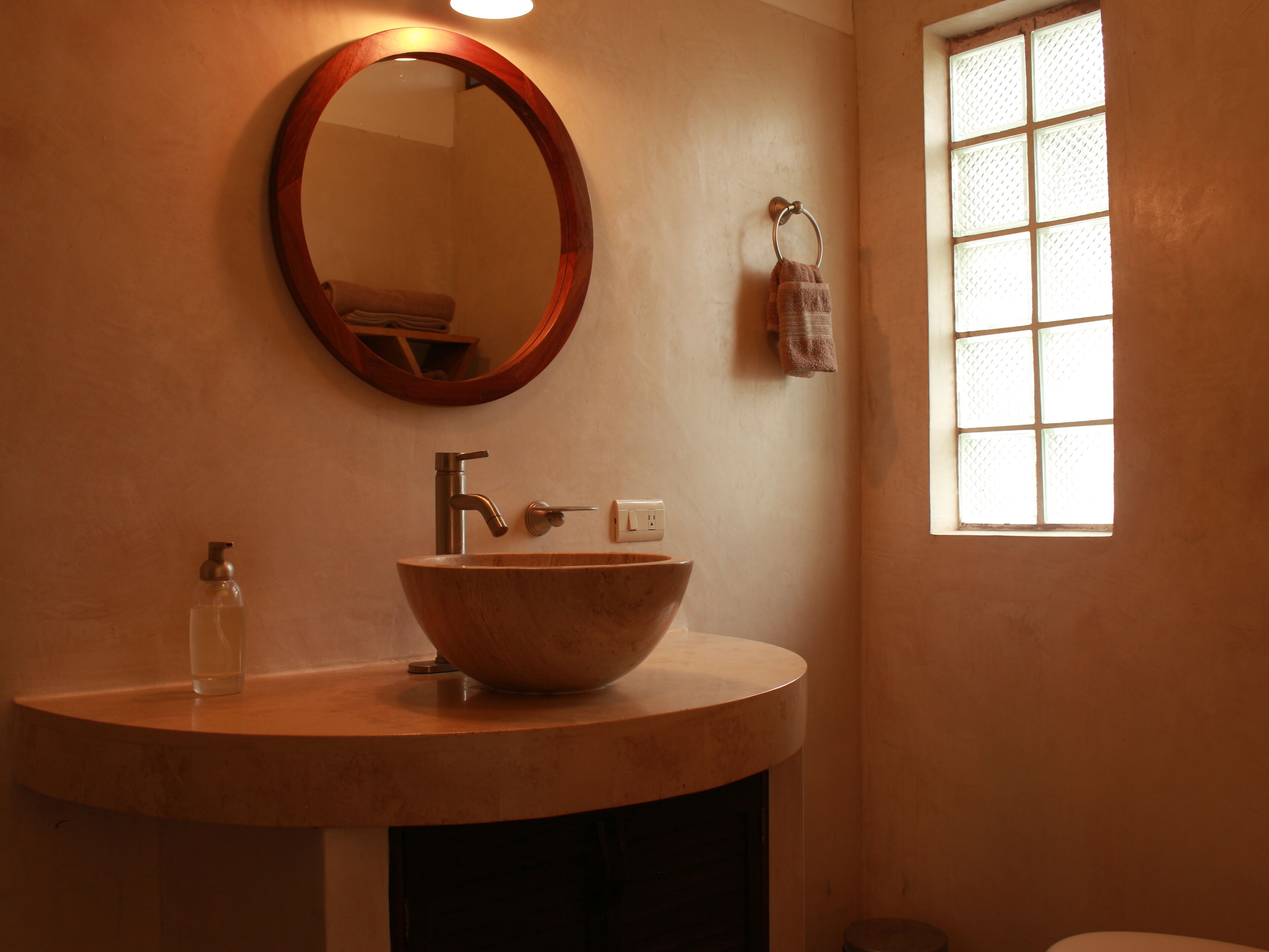 A bathroom with a round mirror, a wooden sink, a towel rack, and a window with a grid pattern.