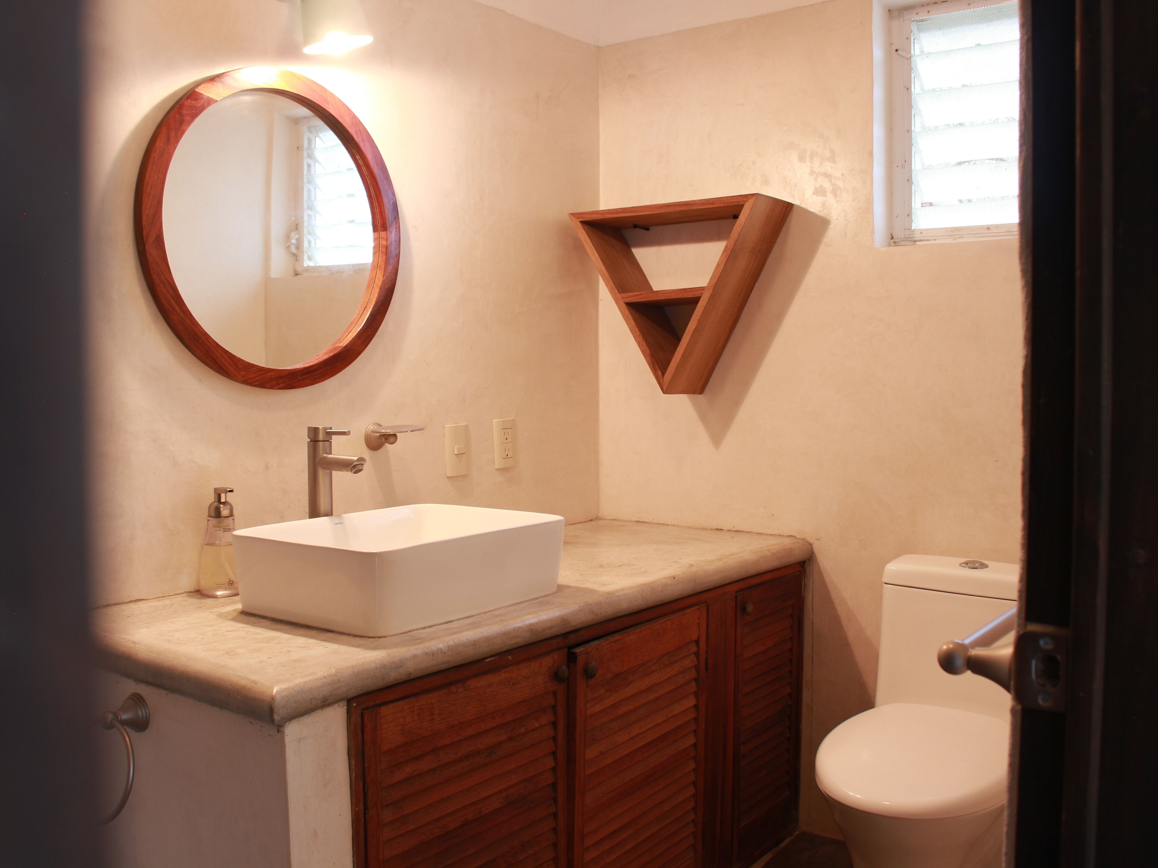 Une salle de bain avec un lavabo blanc, des meubles en bois, un miroir avec un cadre en bois et des toilettes.