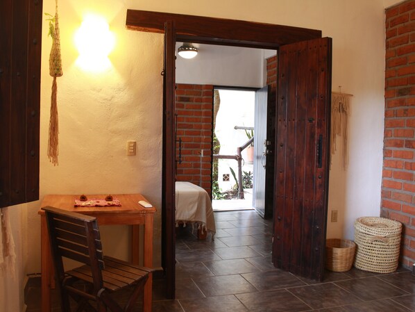 Une table en bois avec une chaise, une plante suspendue et une porte donnant sur un patio aménagé avec une table et des chaises.