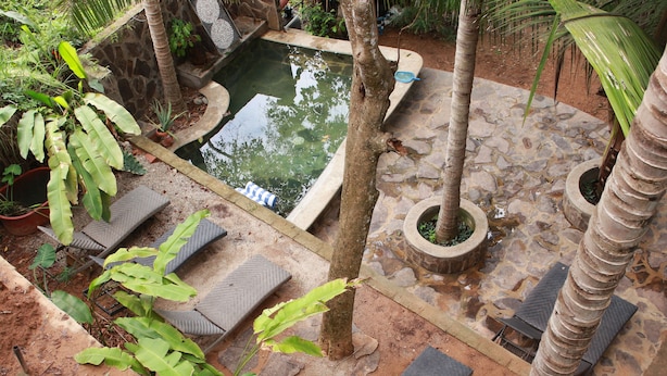 Un espace piscine doté d’un sol en pierre, de chaises longues et de plantes tropicales.