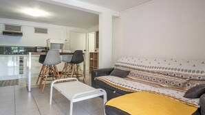 Un salon moderne avec un canapé, une table basse et un coin repas comprenant des chaises, et une cuisine en arrière-plan.