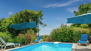 Une piscine rectangulaire à l’eau d’un bleu cristallin, entourée de chaises longues et de parasols, le tout se fondant dans un décor de verdure luxuriante et d’arbres.