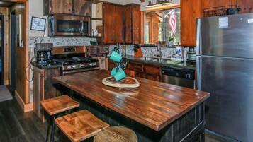 Una cocina con armarios de madera, un refrigerador de acero inoxidable, un microondas y una cafetera. Hay taburetes y una isla de madera con un objeto decorativo.