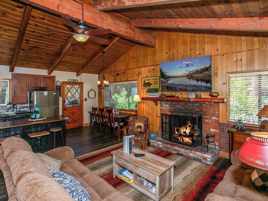 Un intérieur de chalet chaleureux avec une cheminée, des murs en bois, un coin repas et une cuisine équipée d’appareils modernes.