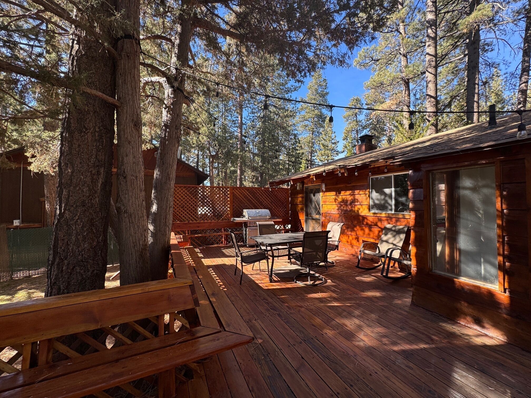 A wooden deck with a barbecue grill, outdoor seating, and a view of tall trees.