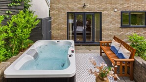 Un bain à remous dans un jardin, avec un banc en bois et un tapis à motifs.