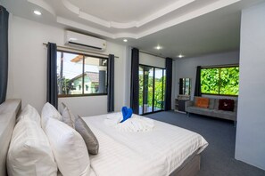 A modern hotel room with a large bed, a sofa, and a balcony with a view of greenery. - 3 Bed 3 Bath Villa 400m to the Beach Sleeps 10 (Choeng Thale)