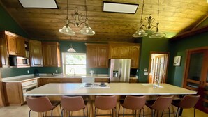 A spacious kitchen with a large island, wooden cabinets, and a stainless steel refrigerator.