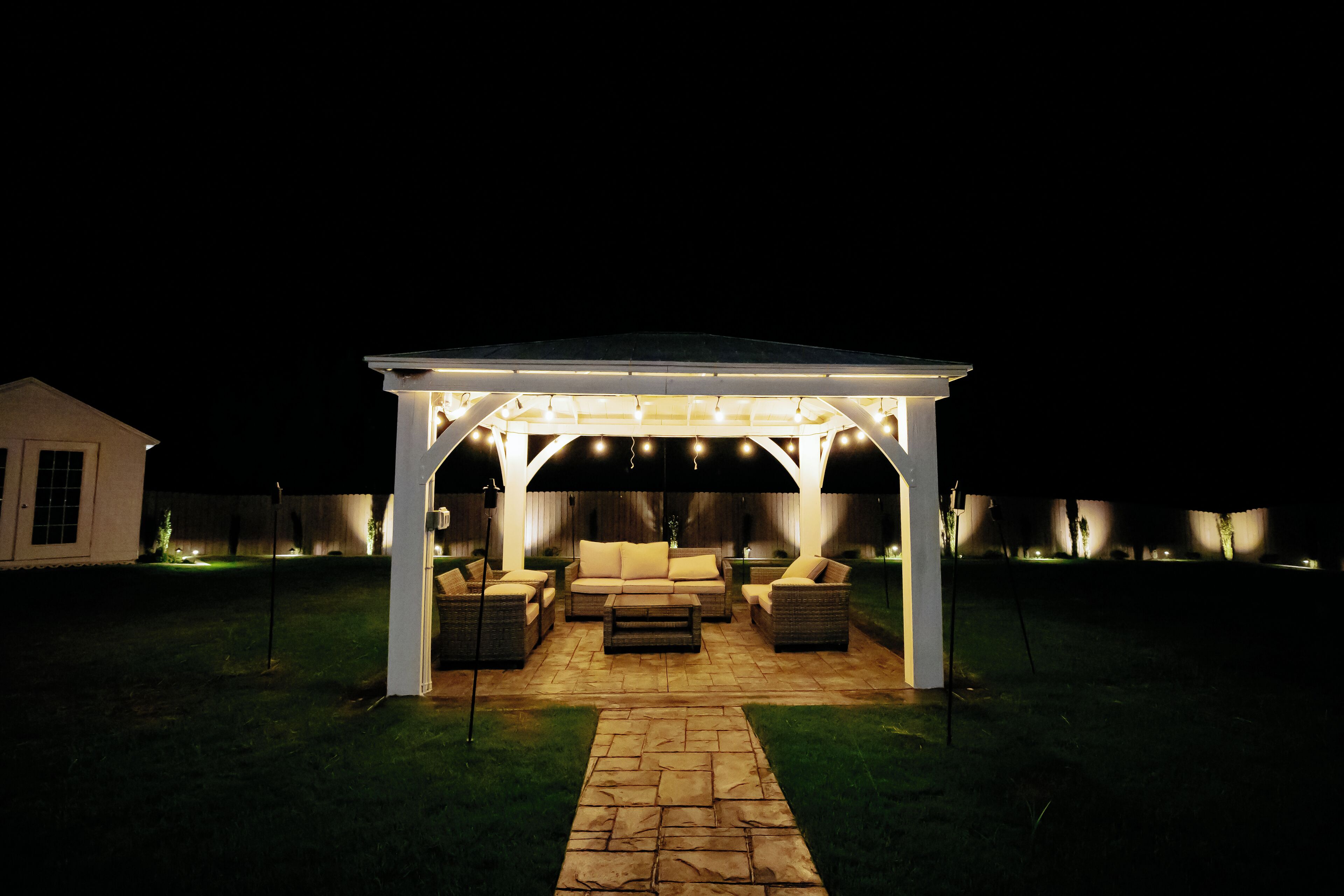 A covered outdoor seating area with a stone pathway leading to it, furnished with sofas and a coffee table.