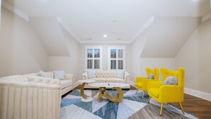 Un loft spacieux avec un plafond haut, un canapé beige, des chaises jaunes et un tapis à motifs.