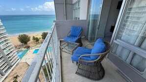 A balcony with wicker chairs and a glass table, overlooking a beach and a pool. - CB171- Beautiful Ocean View With One Bedroom (Carolina)