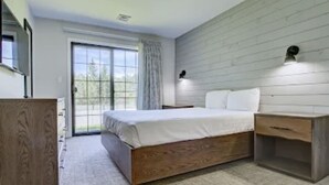 Un dormitorio con una cama de madera, una mesita de noche, un aparador y un ventanal corredero que da a un balcón.