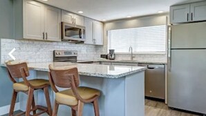 Una cocina moderna con una isla central, taburetes de bar, electrodomésticos de acero inoxidable y armarios azul claro.