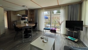 Ein modernes Wohnzimmer mit Essbereich, einem Fernseher auf einem Schrank und einer Schiebeglastür zu einem Außenbereich.