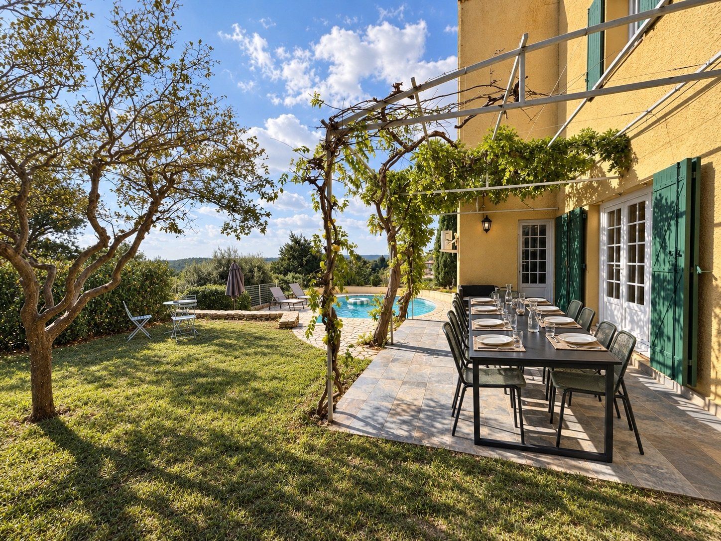 A patio with a table set for dining, a swimming pool, and a view of the surrounding landscape.