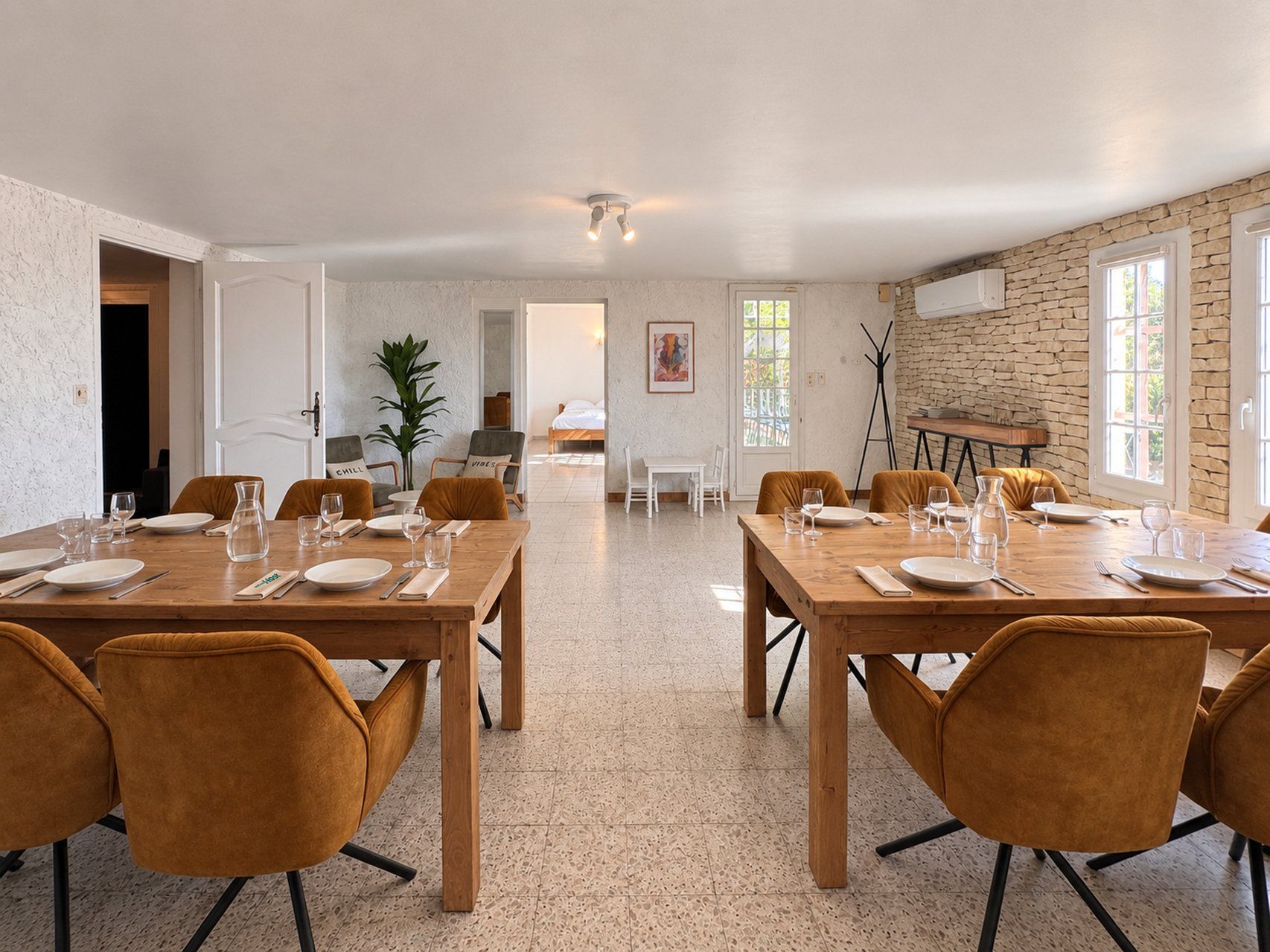 Uma sala de jantar ampla com duas longas mesas de madeira, cada uma disposta para seis pessoas, com pratos, copos e talheres.