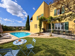 A yellow building with a swimming pool, outdoor seating, and a view of the countryside.