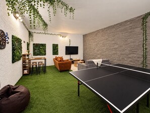 Una stanza con un tavolo da ping pong, un divano, una TV e una parete decorata con piante.