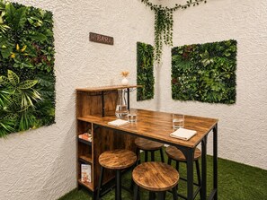 Een houten tafel met krukken, een barbord en groene wanddecoraties.