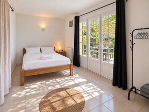 Een slaapkamer met een bed, een bedlamp, een raam met gordijnen, een radiator en een geweven vloermat.