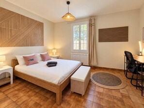 Een slaapkamer met een houten bed, nachtkastjes, een bankje, een bureau en een stoel.