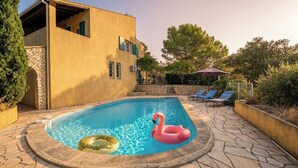 Una piscina con un flotador de flamenco rosa, baldosas de piedra y una pared de piedra.