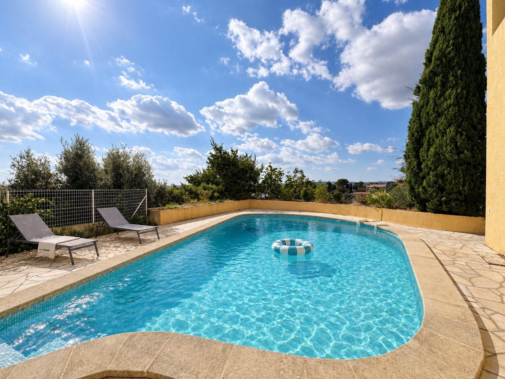 A swimming pool with clear blue water, surrounded by a tiled deck and a fence.