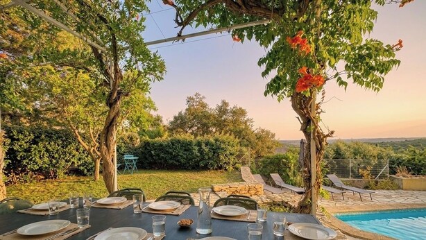 Un espace de restauration en plein air, avec des tables dressées pour un repas, entouré d’une végétation luxuriante et offrant une vue sur une piscine.