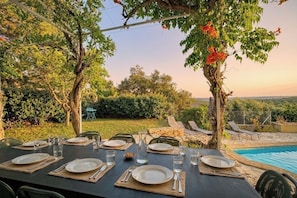 Un espace de restauration en plein air, avec des tables dressées pour un repas, entouré d’une végétation luxuriante et offrant une vue sur une piscine.