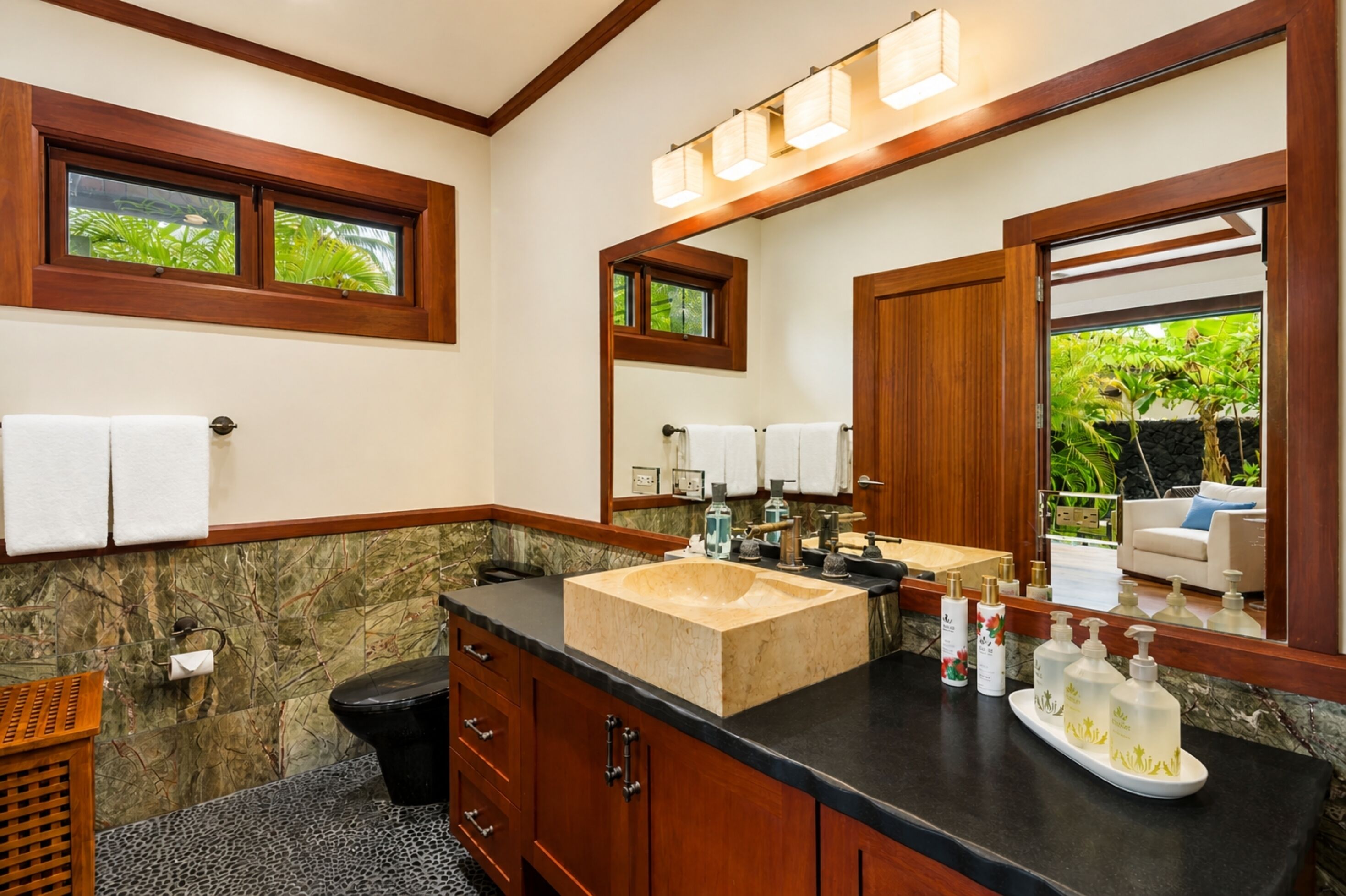 A bathroom with a large mirror, wooden cabinetry, a beige sink, and a black countertop.