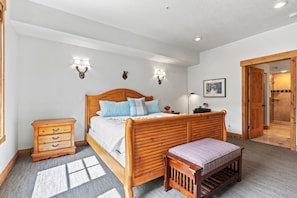 A bedroom with a wooden bed, bedside tables, a bench, and a shower area. - Town Pointe Collection by KBM - 2 Units (102c/301c) (Park City)