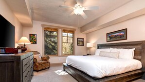 A bedroom with a large bed, a desk with a lamp, a chair, and a ceiling fan. - Town Pointe Collection by KBM - 2 Units (102c/301c) (Park City)