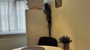 Une table ronde agrémentée de deux sets de table en fibres tressées, d’une plante en pot et d’une lampe fixée au mur.