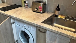 Une cuisine compacte équipée d’un lave-linge intégré, d’un grille-pain et d’un évier.