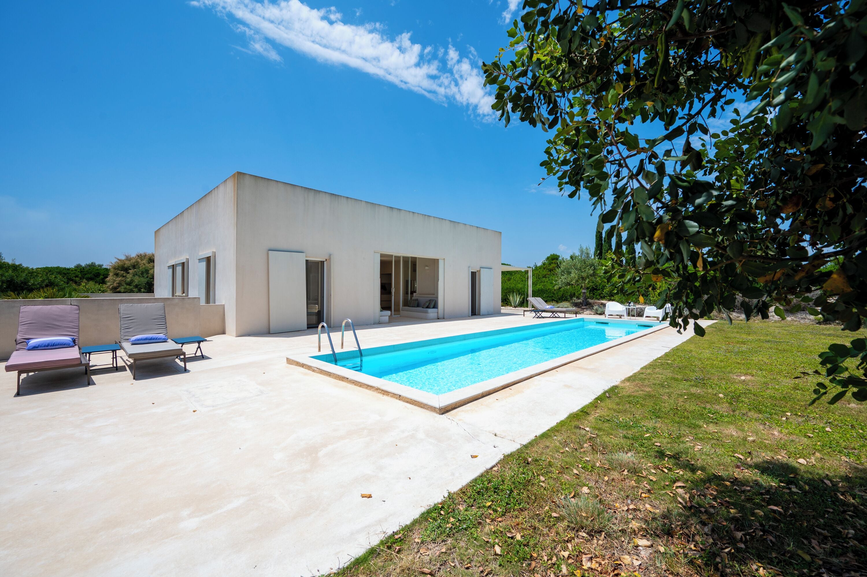 A modern house with a swimming pool, a covered patio with lounge chairs, and a garden.