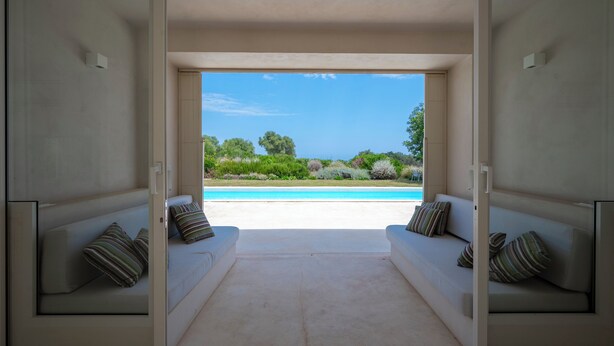 Un espacio de sala de estar abierto con vista a una piscina y vegetación.