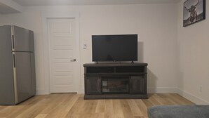 Ein Wohnzimmer mit einem Flachbildfernseher auf einem Holzständer, einem Kühlschrank und einer Tür.