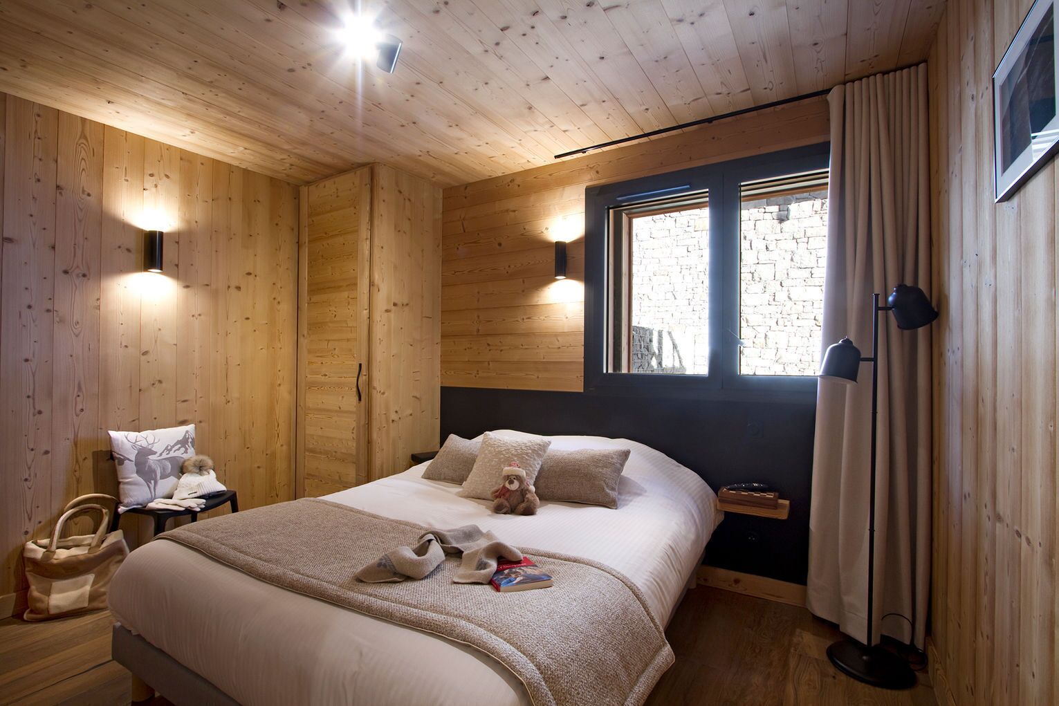 Une chambre à coucher chaleureuse, avec des murs en bois, un lit, des lampes de chevet et une fenêtre avec des rideaux.