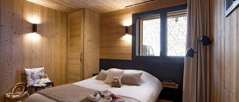 Une chambre à coucher chaleureuse, avec des murs en bois, un lit, des lampes de chevet et une fenêtre avec des rideaux.