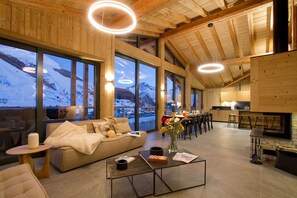 Amplia sala de estar con sofá, mesa de centro y mesa de comedor, ventanas grandes con vista a las montañas y una zona de cocina.