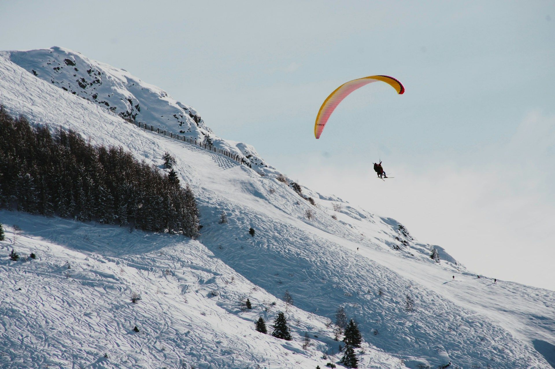 A snowy mountain landscape with a person paragliding.