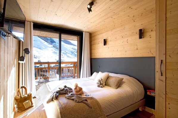 Un dormitorio con una cama grande, techo de madera y vistas a montañas nevadas a través de un ventanal.