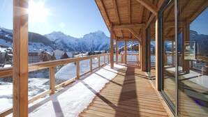 Une terrasse en bois offrant une vue sur des montagnes enneigées et une ville située en contrebas.