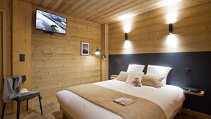 Une chambre à coucher aux murs lambrissés, avec un lit, un téléviseur fixé au mur et une petite table de chevet.
